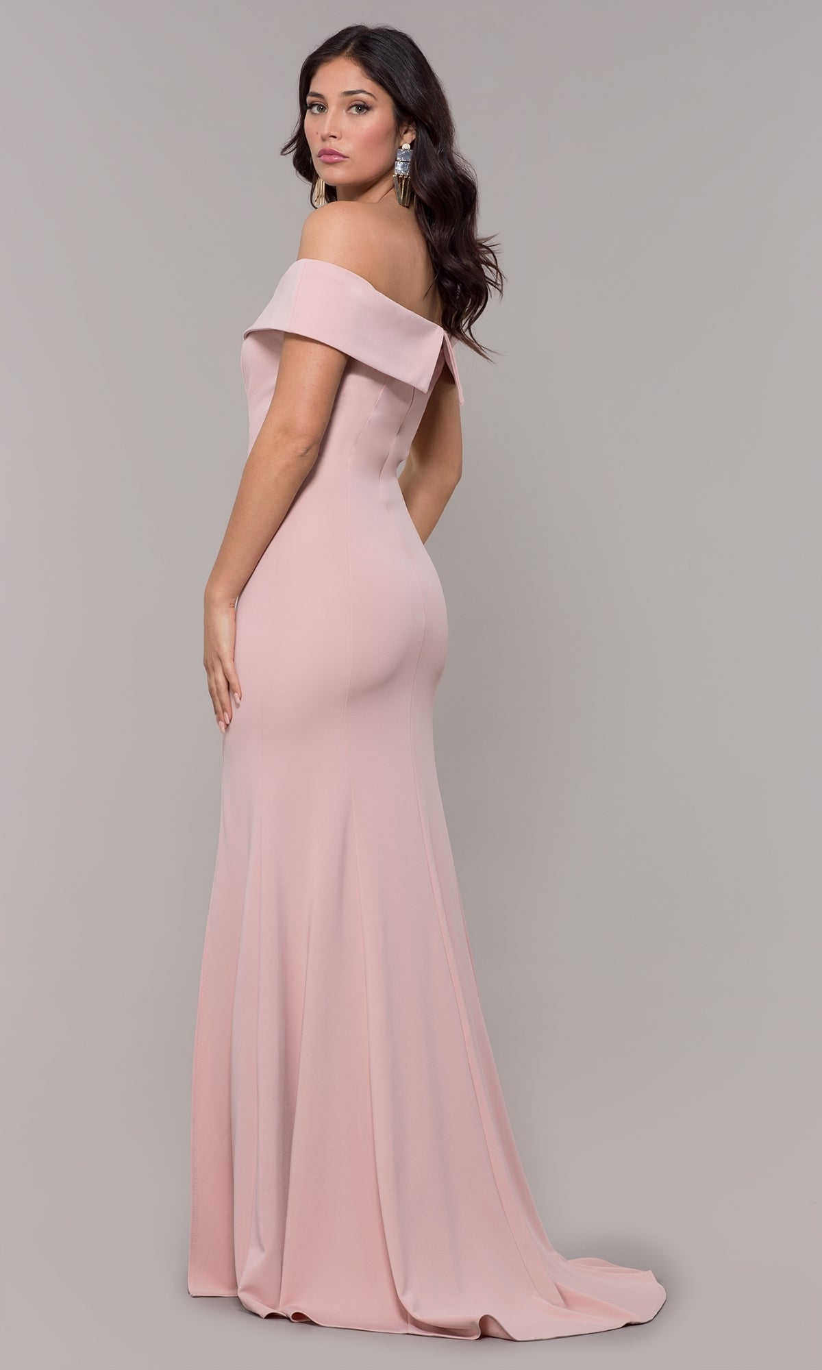 A woman models the Classic Off-the-Shoulder Formal Prom Dress 8258 in light pink, featuring a floor-length design, as she poses against a plain gray background looking over her shoulder.